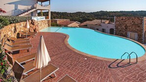 A swimming pool with a curved edge, surrounded by a brick patio, lounge chairs, and umbrellas. - Apartment in Golfo Aranci with terrace (Baja Sardinia (SS))