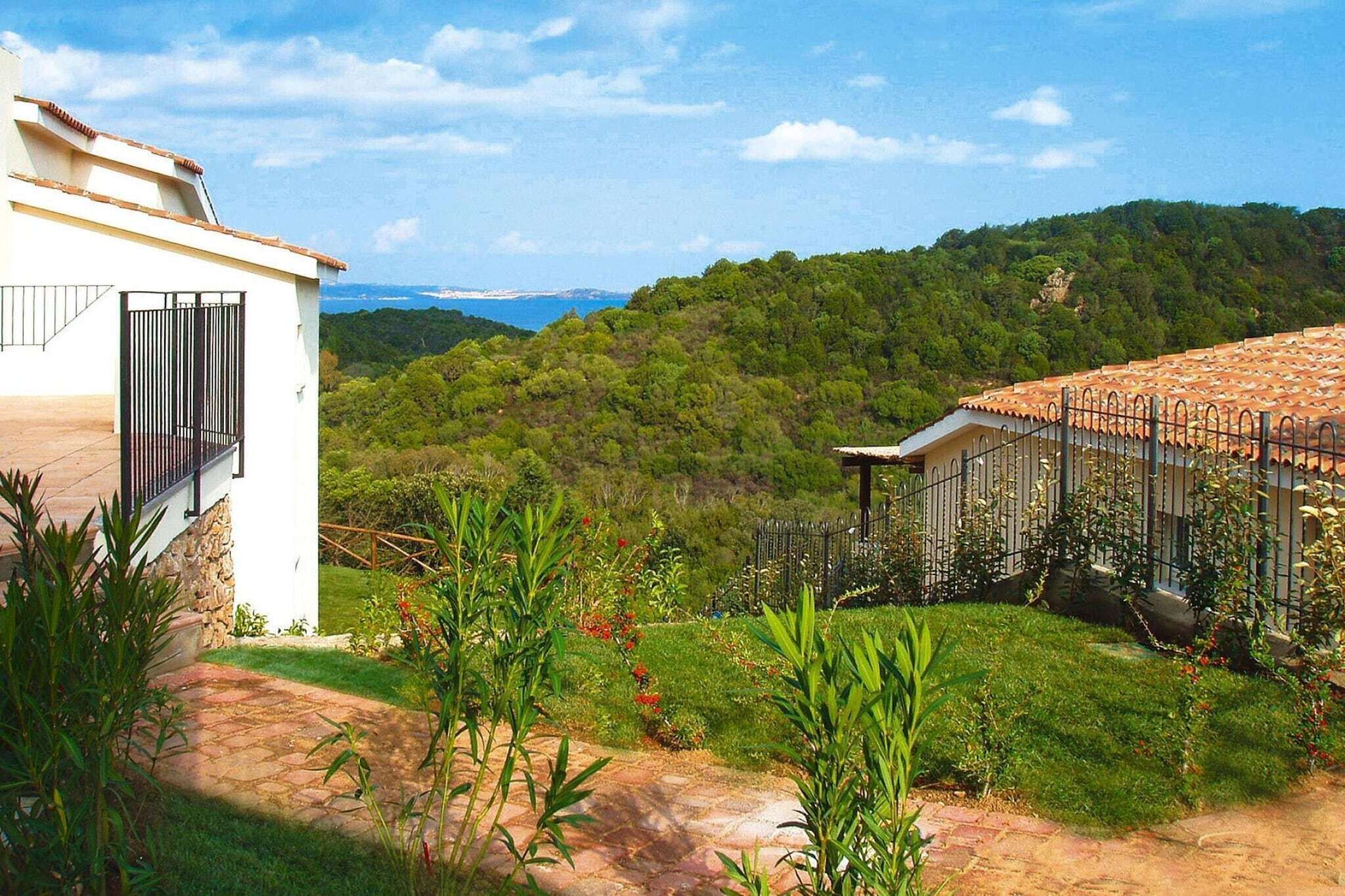 Um bairro residencial com um prédio branco, um jardim cercado e vista para uma colina arborizada.