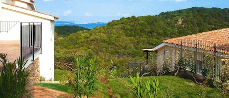 Un barrio residencial con un edificio blanco, un jardín cercado y vistas a una colina boscosa.