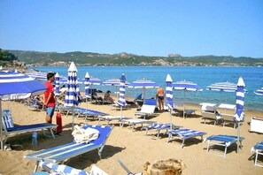 Een strand met rijen ligbedden en blauw-witte parasols.