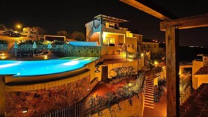 A multi-level building with a swimming pool, outdoor lighting, and a stone wall. - Apartment in Golfo Aranci with terrace (Baja Sardinia (SS))