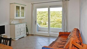 Une pièce comprenant un canapé, un meuble, une télévision et un balcon donnant sur un espace verdoyant.