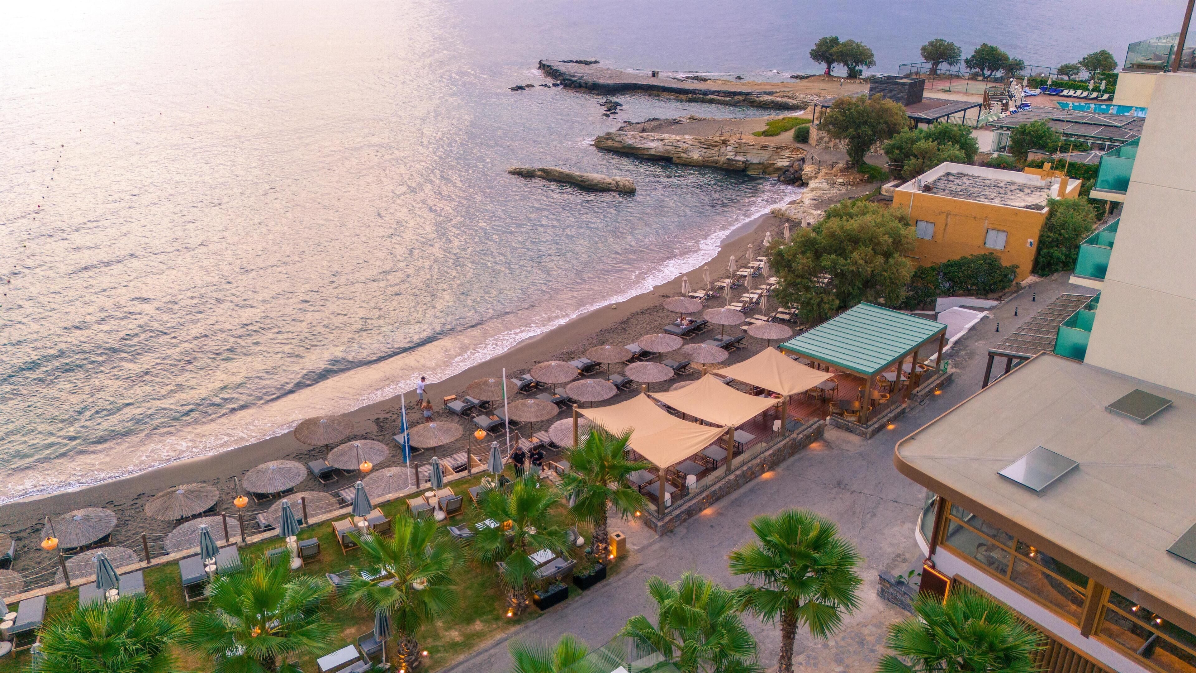 A coastal hotel with outdoor seating, a beach view, and a rocky shoreline.