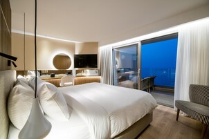 A modern hotel room with a large bed, a desk, a chair, and a balcony with a view.