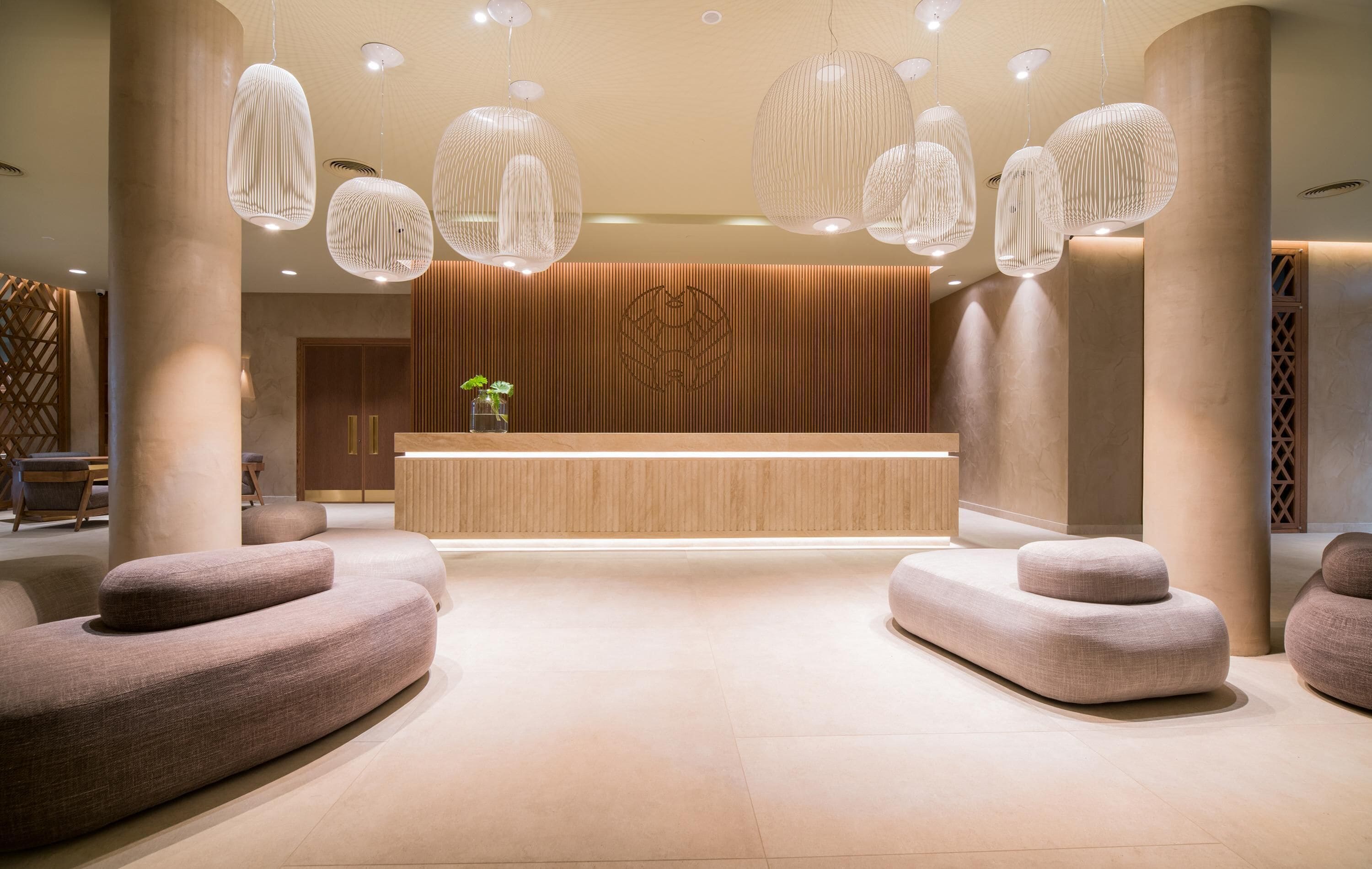 Un área de recepción moderna con un mostrador de madera, grandes columnas y lámparas colgantes tejidas únicas.
