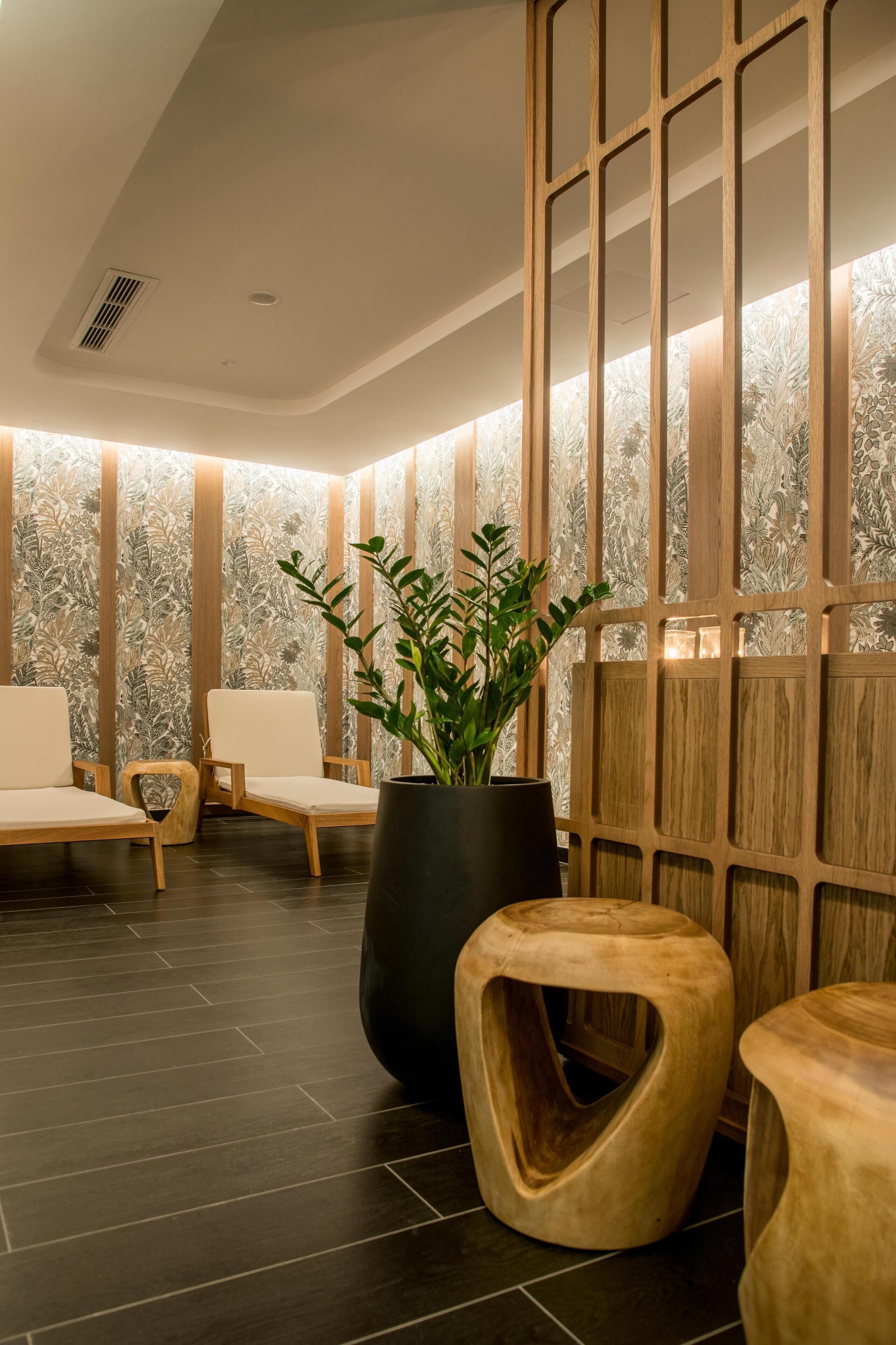 Un área de espera moderna con separadores de madera, sillas con reposabrazos y una planta en maceta.