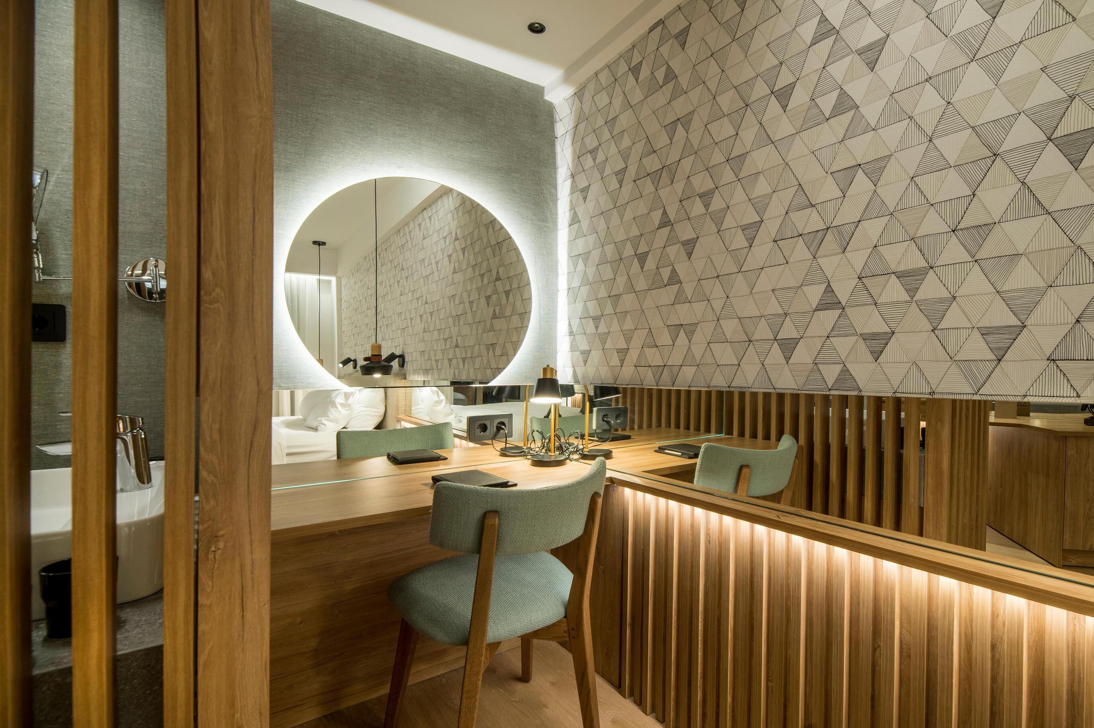 A modern bathroom with a wooden vanity, a round mirror, and a geometric patterned wall.