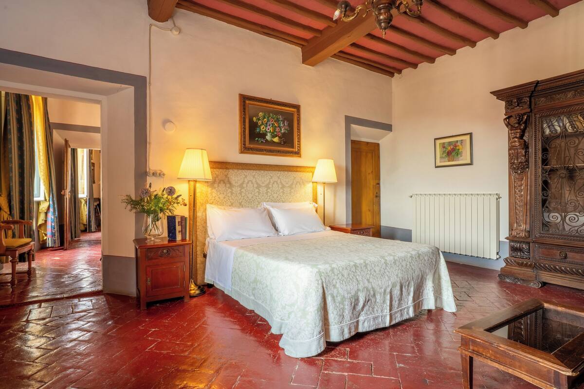 Une chambre spacieuse avec un grand lit, une tête de lit en bois, deux lampes de chevet et une commode en bois.