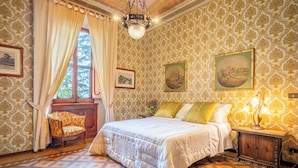 Ein Schlafzimmer mit gemustertem Wandpapier, einem großen Bett mit weißer Bettdecke, einem Nachttisch aus Holz mit einer Lampe und einem Sessel.