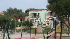 A playground with swings, a slide, and a climbing structure. - Apartment in Badus with communal Pool (Badesi)