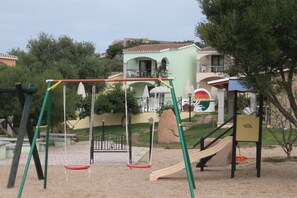 A playground with swings, a slide, and a climbing structure. - Apartment in Badus with communal Pool (Badesi)