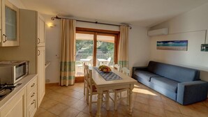A compact kitchen with a microwave, a dining table with chairs, and a sofa. - Apartment in Badus with communal Pool (Badesi)