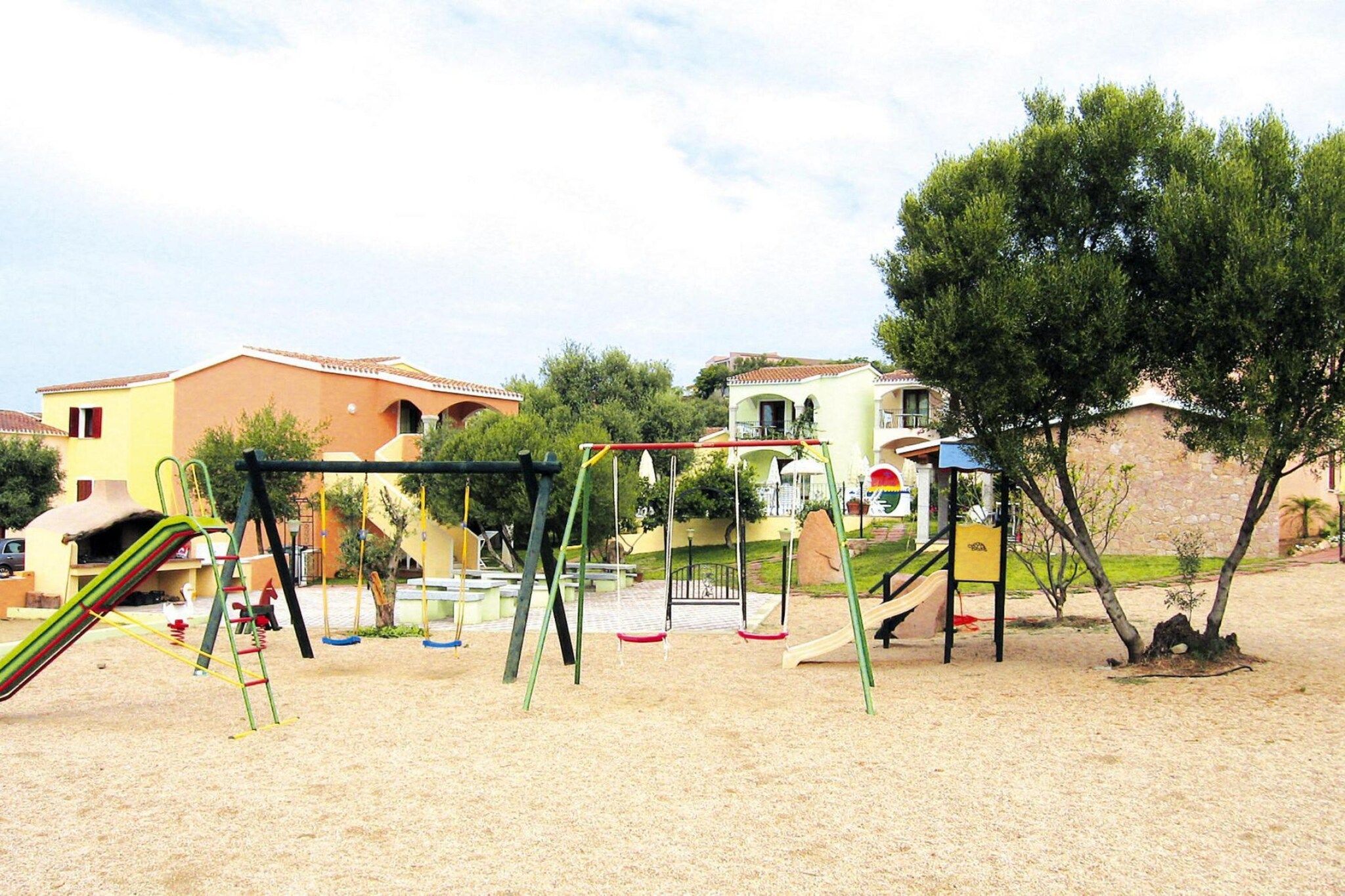 A playground with swings and a slide, surrounded by buildings and trees.