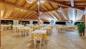 A spacious dining area with multiple tables and chairs, a high wooden ceiling, and ceiling fans. - Apartment in in Badesi with Shared Pool (Badesi)