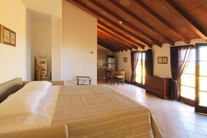 A bedroom with a large bed, wooden ceiling beams, a desk, and a view of the kitchen. - Terrace Vibes in the Italian Sun (Piombino)