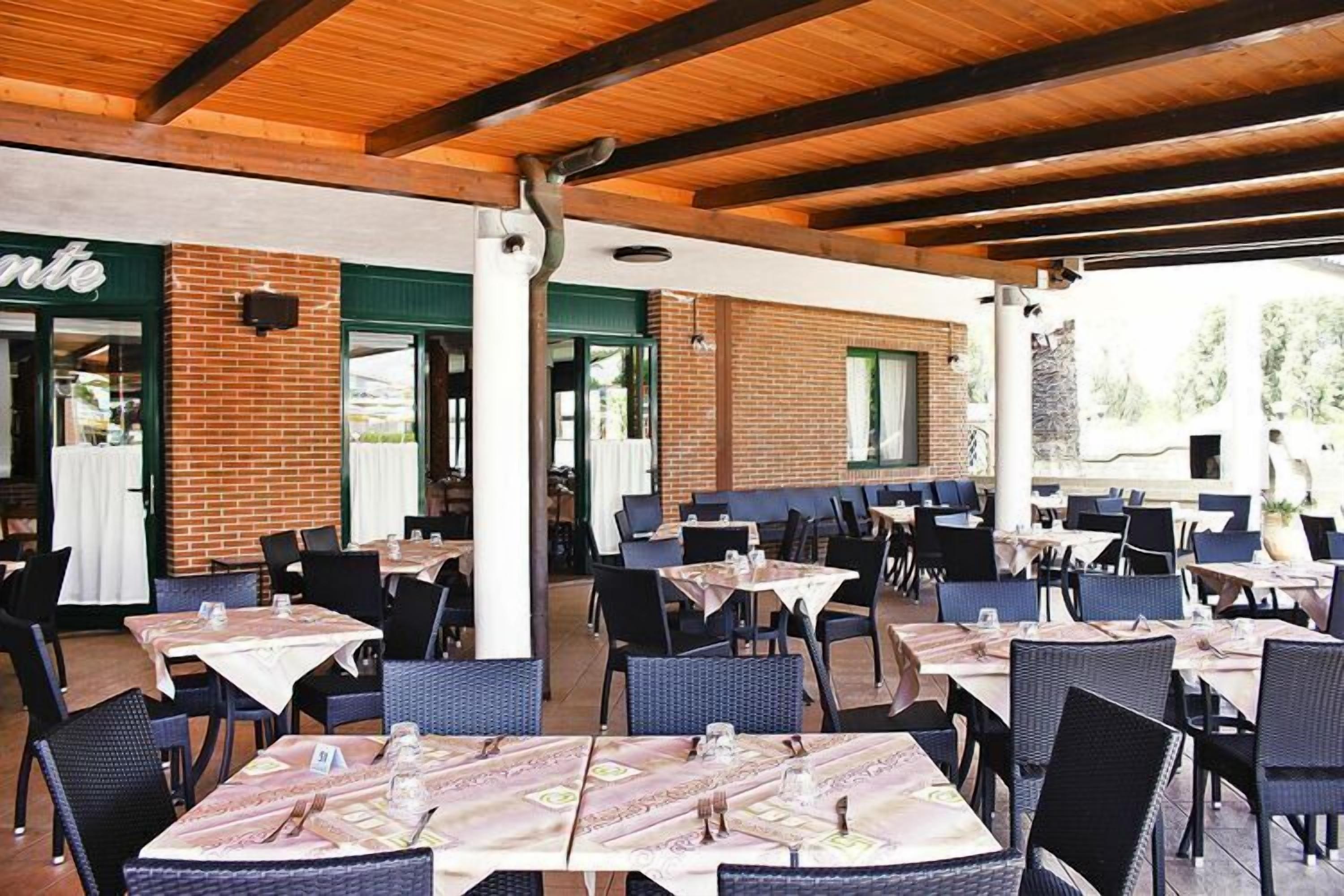 Un restaurante al aire libre con paredes de ladrillo, vigas de madera y mesas preparadas para comer.