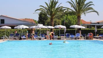 Une piscine avec des chaises longues et des parasols, des palmiers et un bâtiment en arrière-plan.