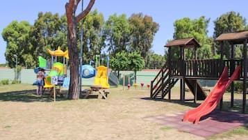 A playground with slides and climbing structures, surrounded by trees and a wooden fence.