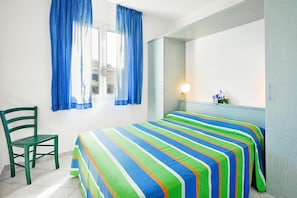 A room with a bed, a chair, a window with curtains, a bedside table with a lamp, and a mirror. - Villa in Cecina Mare near Sandy Beach (Cecina Mare)
