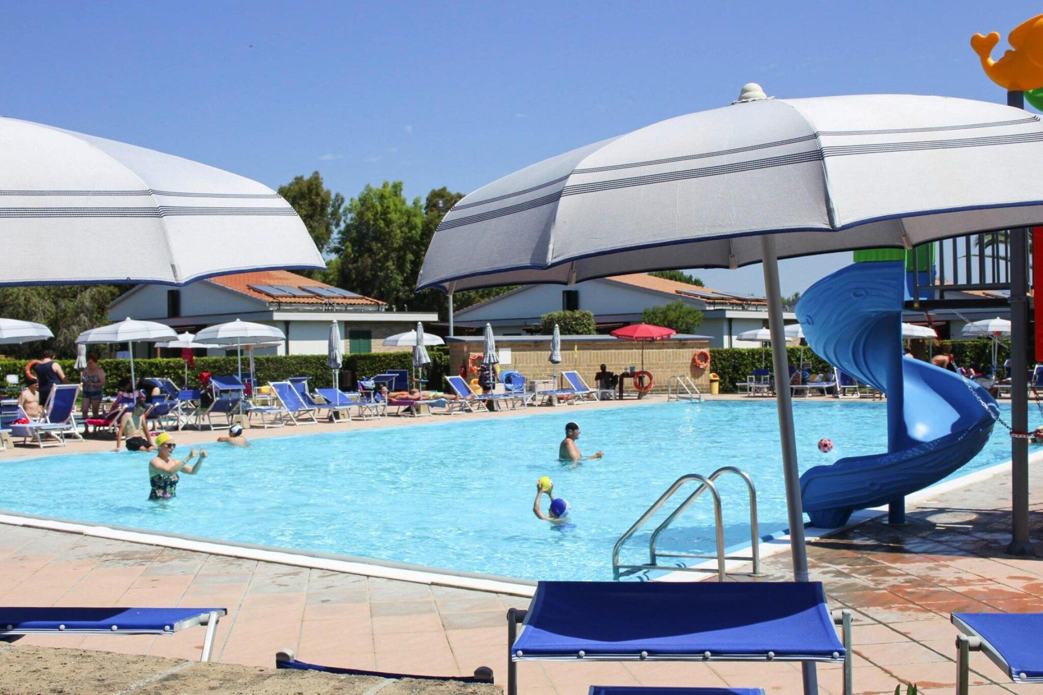 A swimming pool with lounge chairs and umbrellas, a water slide, and a lifeguard stand.
