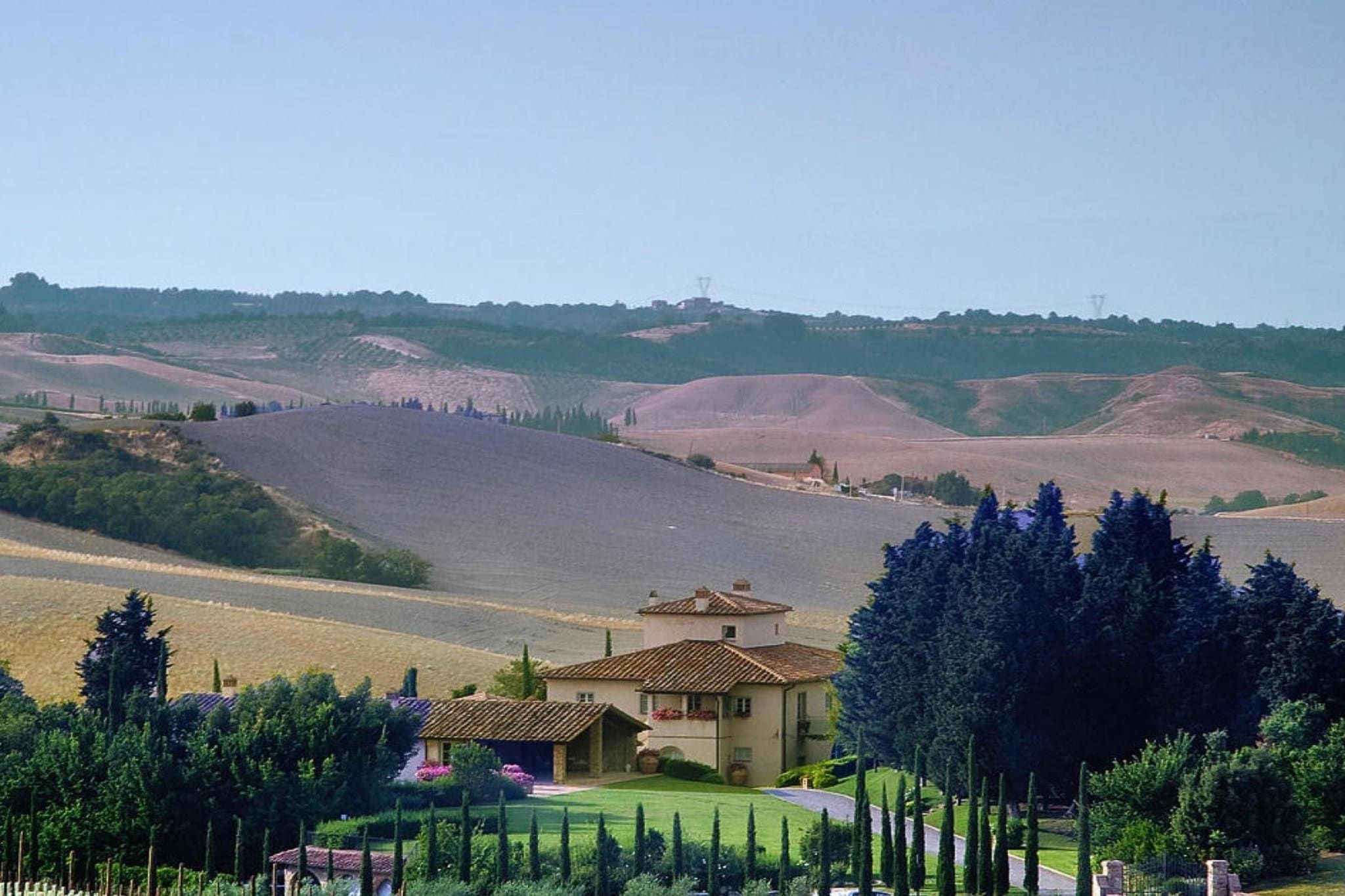Un paysage rural avec des collines ondoyantes, une maison avec un toit en tuiles et un ciel dégagé.