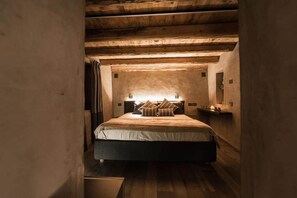 A cozy, dimly lit bedroom with a wooden ceiling, a large bed with pillows, and a bedside table with a lamp. - Relais Bondaz (Aosta)
