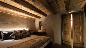 Een slaapkamer met een houten plafond, een bed met gestreepte kussens, een nachtkastje met een lamp en een houten deur.
