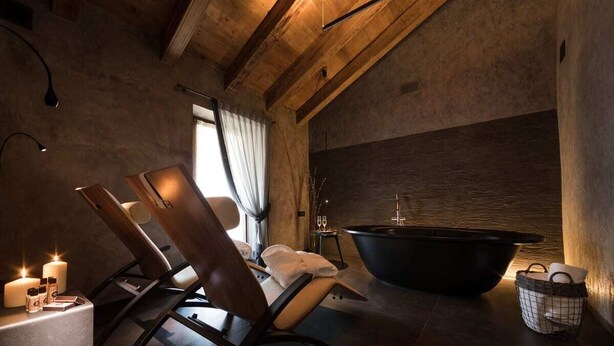 Een spa-ruimte met een houten plafond, een zwart bad en twee stoelen.