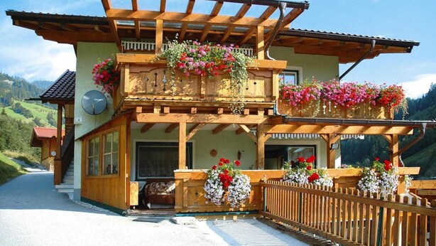 A wooden chalet with a balcony adorned with flowers, a wooden fence, and a scenic mountain backdrop. - Chalet in Grossarltal with Panoramic Views (Großarl)