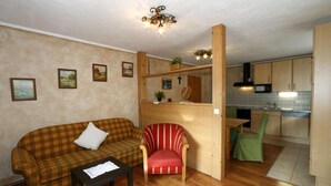 A compact living space with a sofa, armchair, small table, kitchenette, and wooden flooring. - Chalet in Grossarltal with Panoramic Views (Großarl)