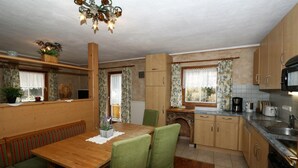 A compact kitchen with wooden cabinets, a dining table with green chairs, a built-in oven, and a microwave. - Chalet in Grossarltal with Panoramic Views (Großarl)