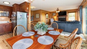 A wooden interior with a dining table, chairs, a refrigerator, a microwave, and a fireplace. - Skyview Cabin - Spectacular View, 2 BR, 2 1/2 BA, Brand New Hot Tub, Firepit (Maggie Valley)
