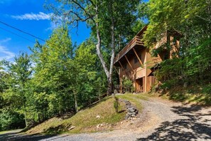 A rustic cabin with a wooden deck, surrounded by dense forest. - Skyview Cabin - Spectacular View, 2 BR, 2 1/2 BA, Brand New Hot Tub, Firepit (Maggie Valley)