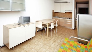 A compact kitchen with a dining table, chairs, a small refrigerator, and a television on a cabinet.
