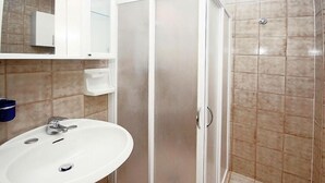 A bathroom with a white sink, a mirror, a cabinet, and a shower area.