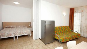 A room with a bed, a sofa, a refrigerator, and a dining table.