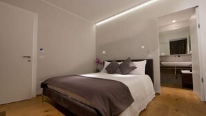 A modern bedroom with a bed, a nightstand, and a bathroom visible through an open door. - MaVille (Aosta)
