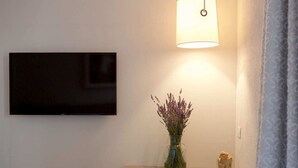 A room with a flat-screen TV mounted on the wall, a table with a vase of lavender, and a lamp providing light. - MaVille (Aosta)