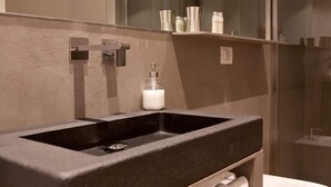 A bathroom with a black sink, a mirror, and a shelf with toiletries. - MaVille (Aosta)