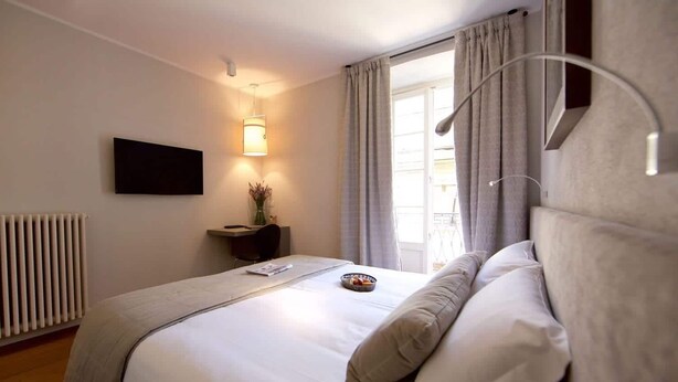 A neatly arranged bedroom with a bed, bedside table, lamp, and a window with curtains. - MaVille (Aosta)