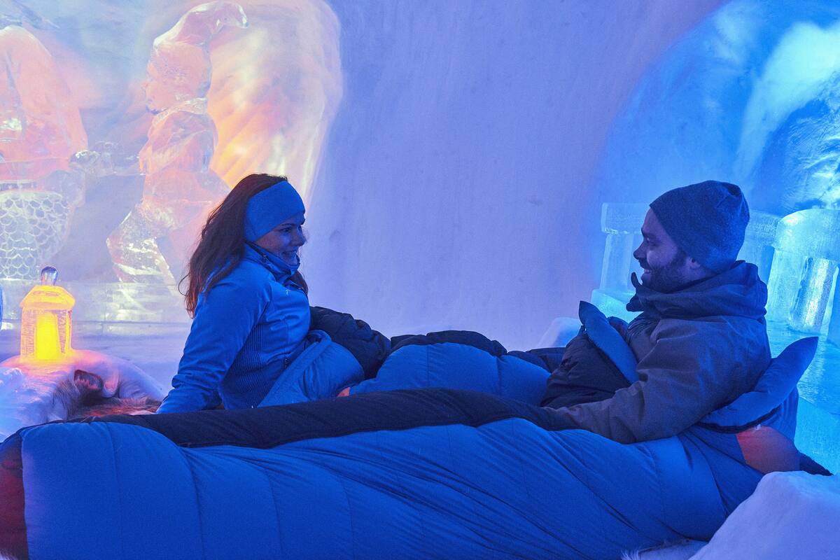 Two people sitting on a bed in a room with ice sculptures and a yellow lamp.