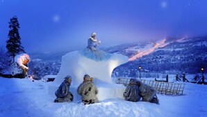 A snow-covered landscape with a large ice sculpture of a figure in a blue dress, surrounded by snowmen and a fence. - Hunderfossen Snøhotell (Lillehammer)