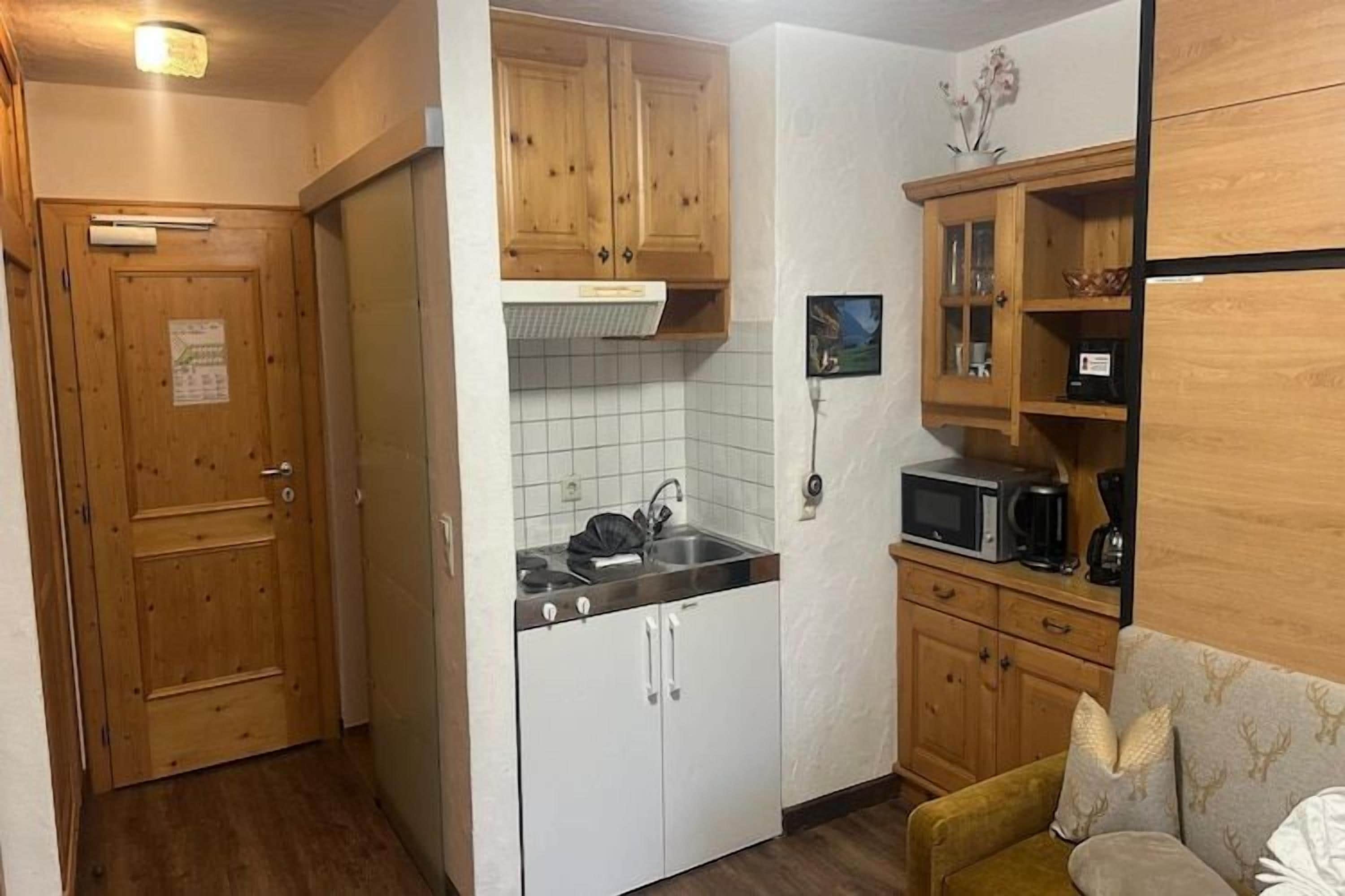Una cocina compacta con muebles de madera, un microondas y un lavabo.