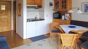 A compact kitchen with a stove, sink, and cabinets, a dining area with a table and chairs, and a television on a wooden cabinet. - Apartment in Wildschönau by Schatzberg Lift (Wildschönau)