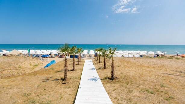 A beach with a wooden walkway leading to white umbrellas and beach chairs. - Hotel Sporting (Casalbordino)