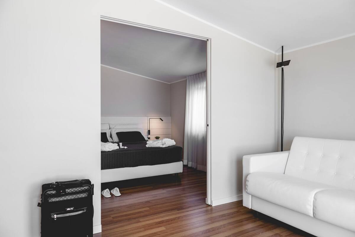 A modern hotel room with a bed, a white sofa, and a suitcase.