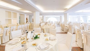 A banquet hall with round tables set for a formal event, featuring white tablecloths, chairs with white covers, and a spacious layout with large windows. - Hotel Sporting (Casalbordino)