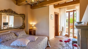 A bedroom with a large bed, a mirror, a chandelier, and a view of the garden through a door. - Mons Major Relais (Colli al Metauro)
