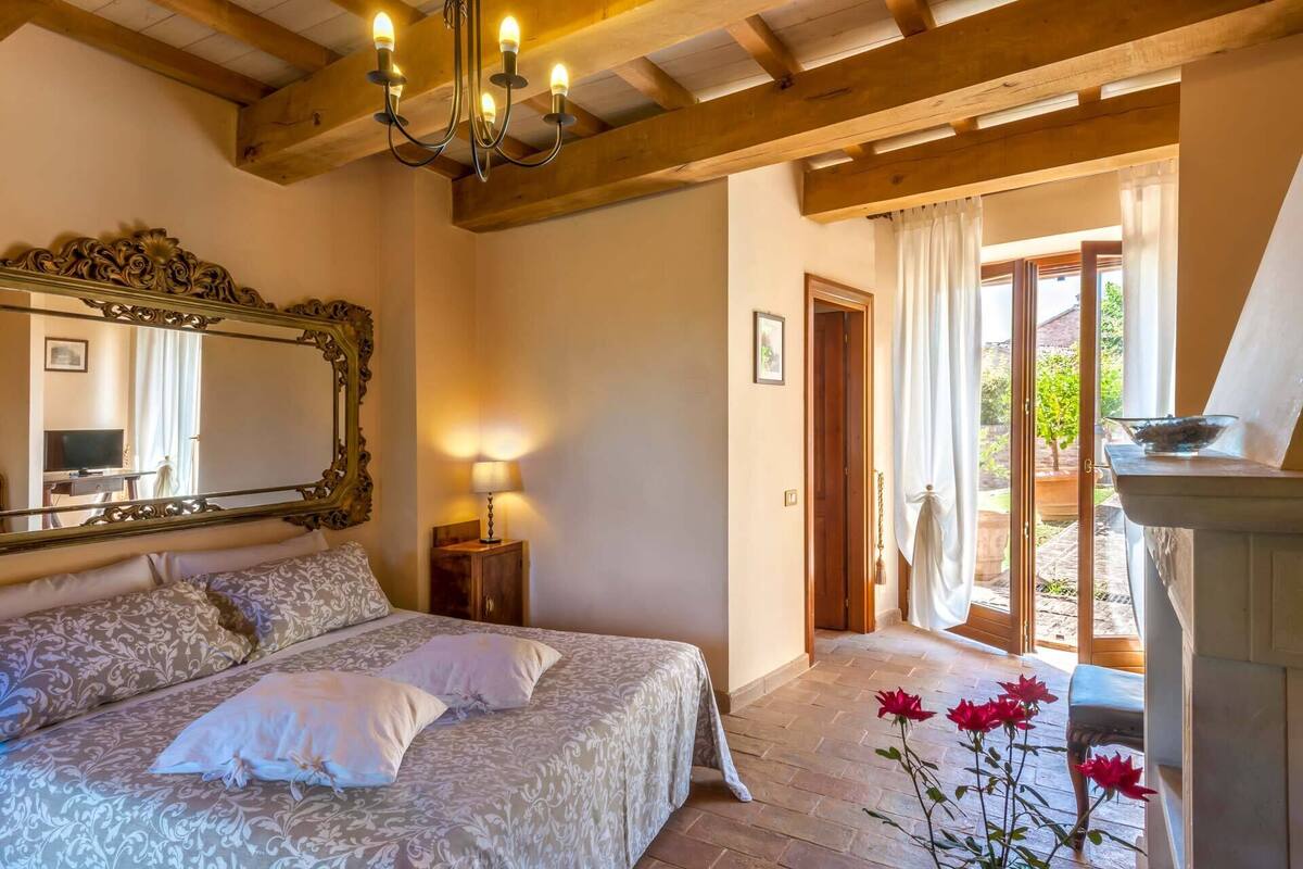 Un dormitorio con una cama grande, un espejo, una araña y vistas al jardín a través de una puerta.
