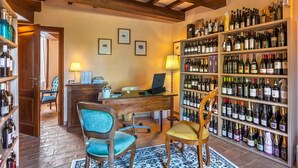 A room with a wooden desk, two chairs, a laptop, and a wall of wine bottles. - Mons Major Relais (Colli al Metauro)